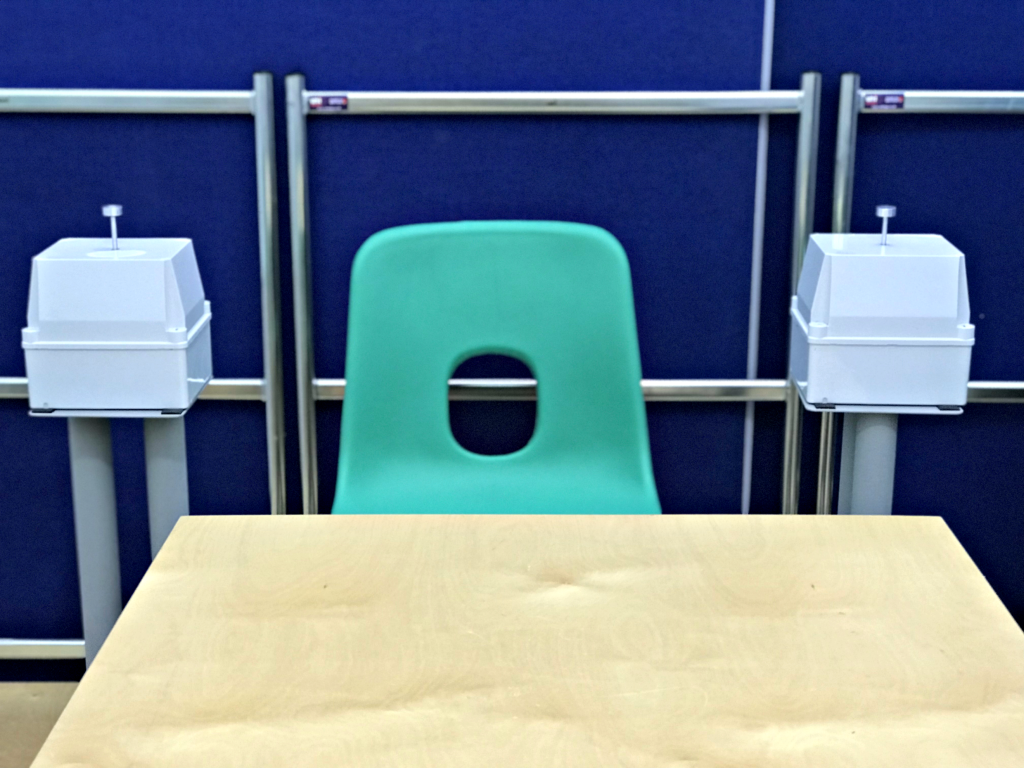 Photo showing a green chair at a wooden table, with a vibrotactile hand shaker placed to either side of the chair.
